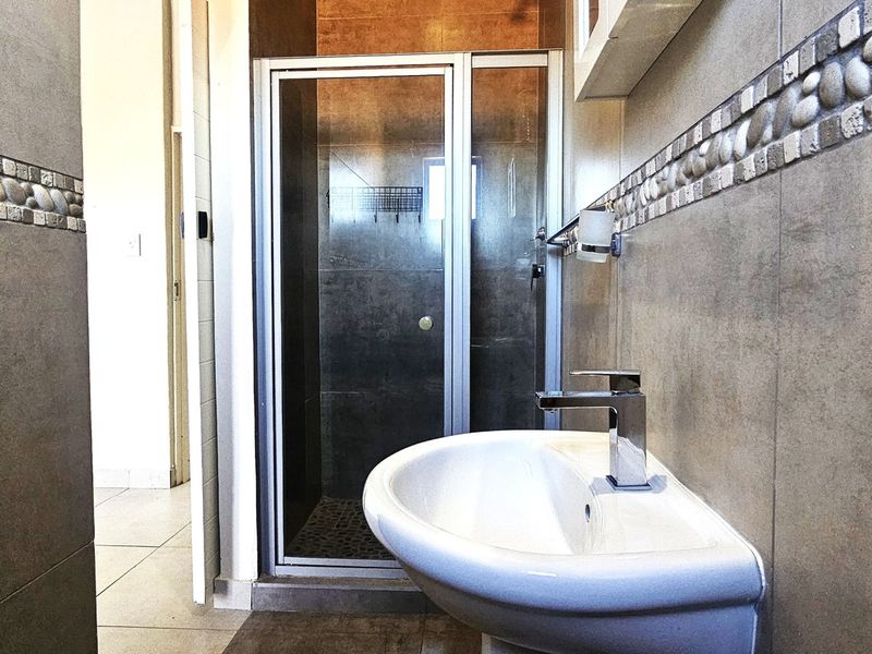 A functional bathroom featuring a pedestal basin with a chrome mixer tap and a separate shower enclosure with tiled walls and decorative border detailing.