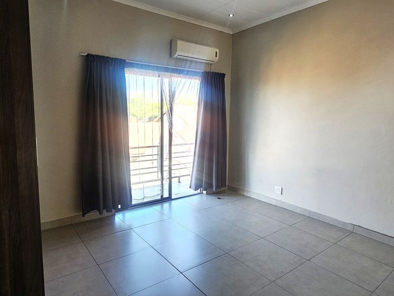 A bright, empty bedroom featuring tiled flooring, a built-in cupboard, and a sliding glass door leading to an outdoor area with air conditioning.