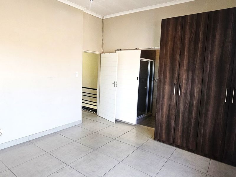 A spacious bedroom featuring neutral tiled flooring, built-in dark wood cupboards, and direct access to an en-suite bathroom.