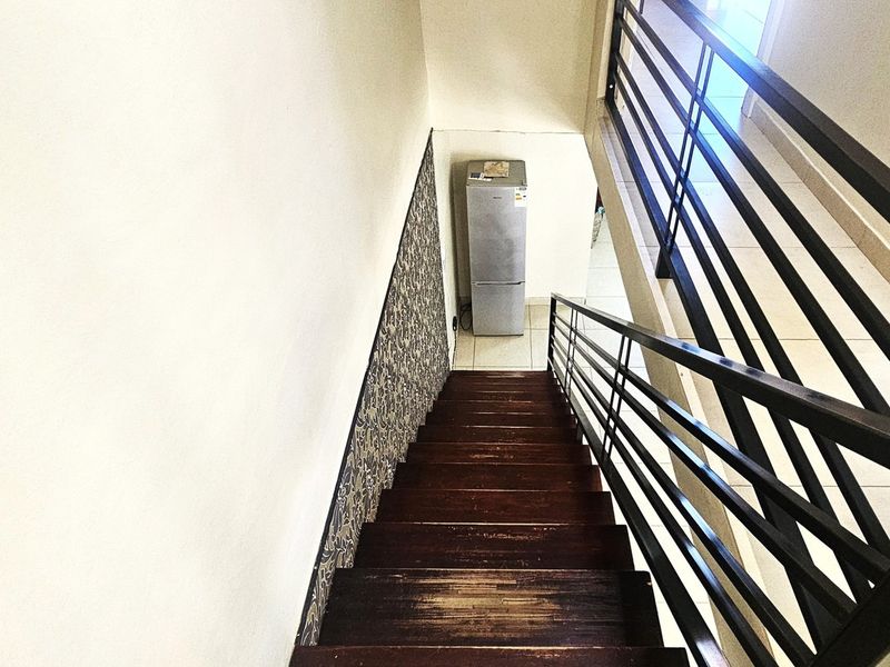 A staircase featuring wooden treads and a black metal balustrade, accented by a section of patterned wallpaper.