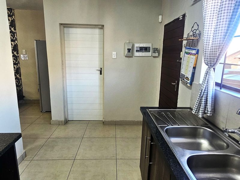A functional kitchen area featuring double bowl stainless steel sink, laminate countertops, tiled flooring, and direct access to adjacent living spaces.