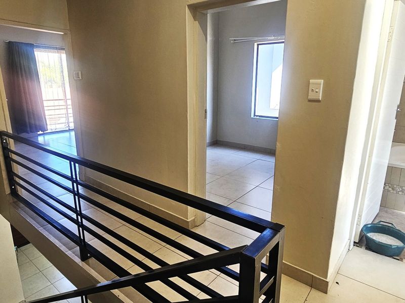 Upper level hallway featuring tiled flooring, a metal balustrade, and access to a bathroom and adjacent bedroom.