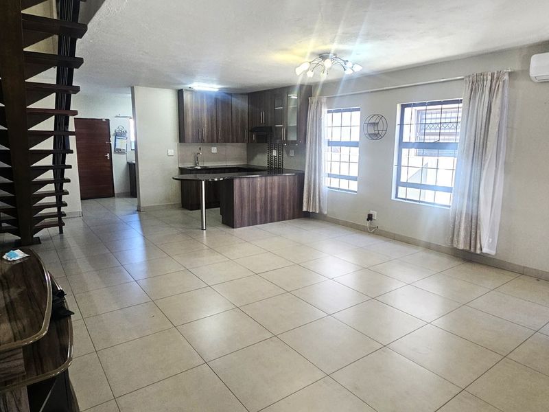 Spacious open-plan living area featuring tiled floors, a modern kitchen with island, and an open-tread staircase leading to the upper level.