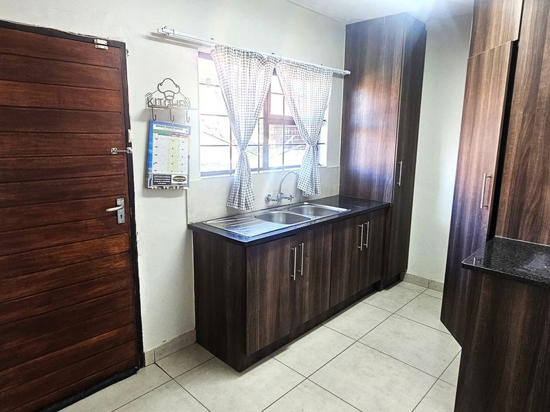 A functional kitchen featuring dark wood cabinetry, laminate countertops, a double sink, and tiled flooring, providing a practical workspace.