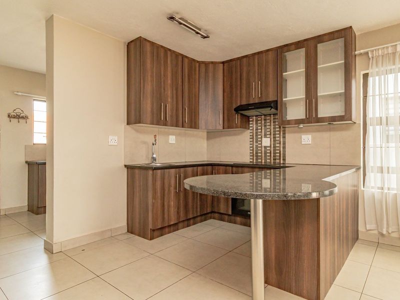 A clean, functional kitchen featuring dark wood-look cabinetry, granite countertops with an integrated breakfast bar, and neutral tiled flooring.