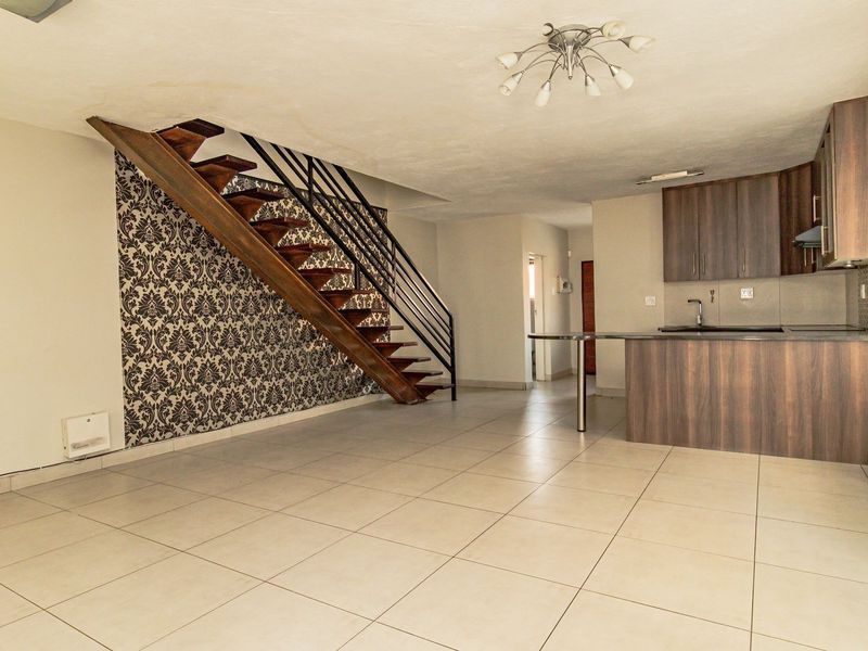 Open-plan living area featuring a modern staircase with metal balustrade, tiled flooring, and a functional kitchen with built-in cabinetry and island.