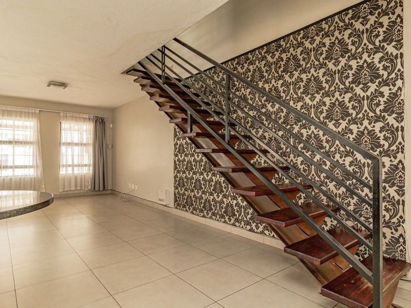 Open-plan living area featuring a distinctive open-tread staircase with metal balustrade, tiled flooring, and a decorative feature wall.