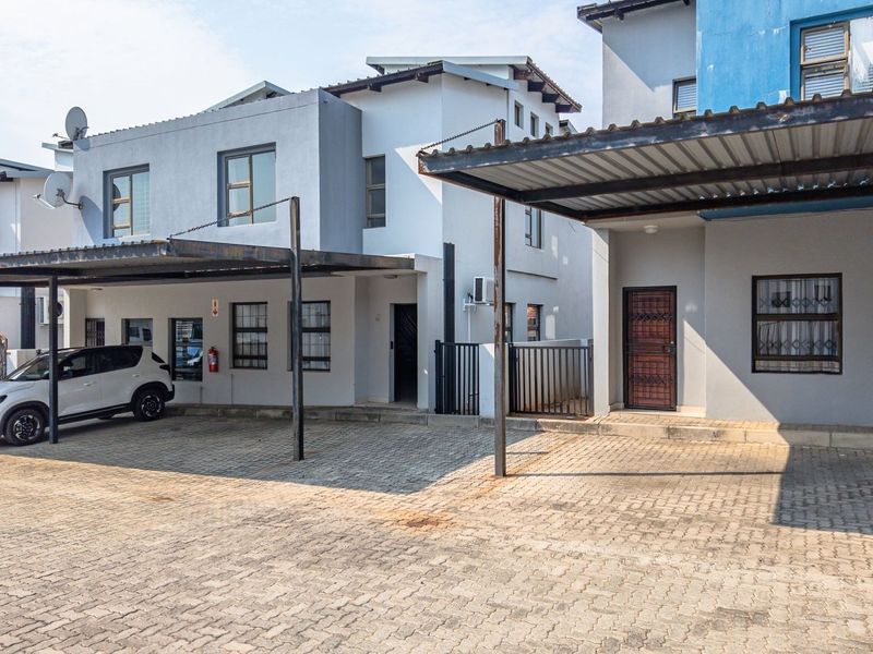 Front exterior view of a townhouse complex featuring paved driveway parking, covered carports, and security features including bars and gates.
