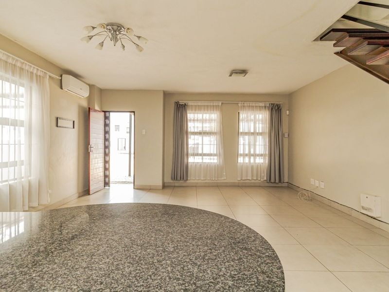Spacious open-plan living area featuring tiled floors, a granite breakfast bar, split-system air conditioning, and a staircase leading to the upper level.