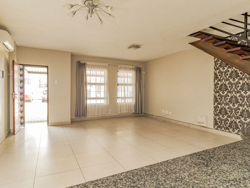 Spacious open-plan living area featuring tiled floors, a modern staircase, and a granite breakfast bar, offering a bright and versatile layout.