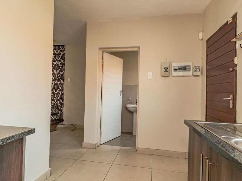 A functional kitchen area featuring granite countertops, stainless steel sink, and tiled flooring, with an adjacent doorway leading to a small bathroom.