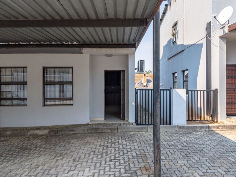 Front exterior view of the townhouse featuring a covered carport, paved driveway, and secure gated entrance.