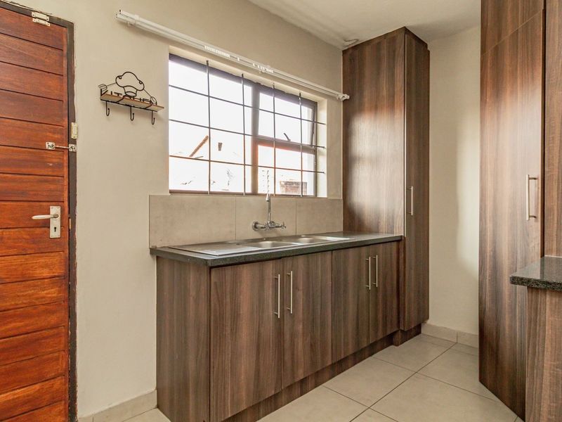 A functional scullery featuring dark wood-look cabinetry, laminate countertops, a stainless steel sink, and tiled flooring, providing additional prep and storage space.