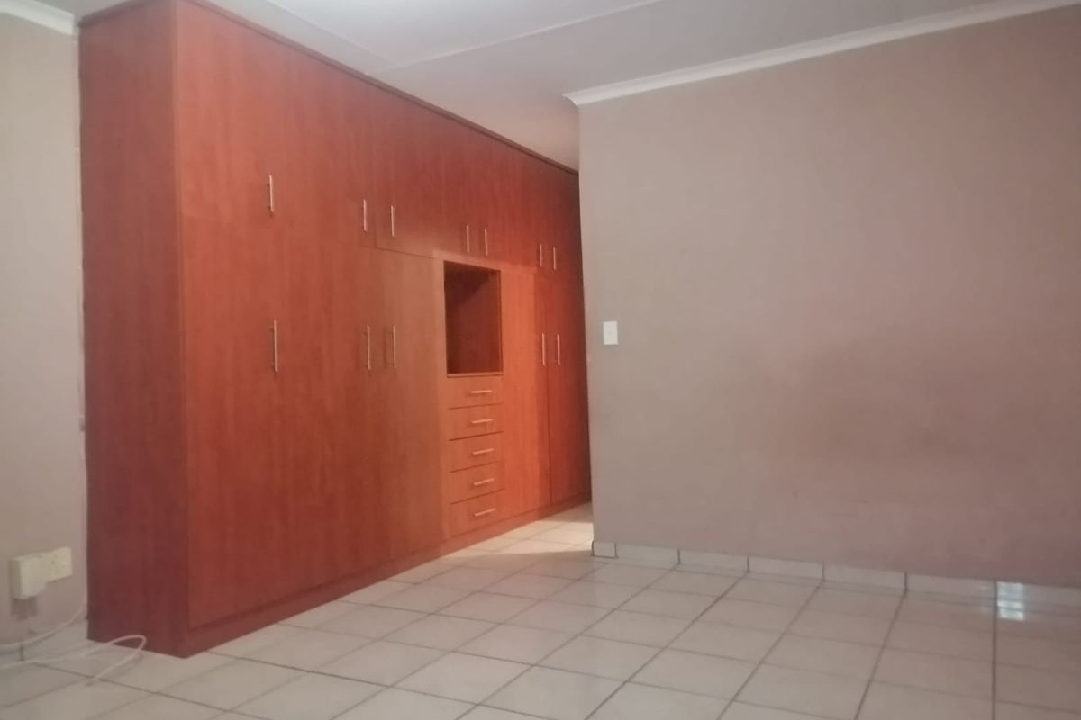 A spacious bedroom featuring extensive built-in wooden cabinetry, neutral wall finishes, and durable tiled flooring throughout.