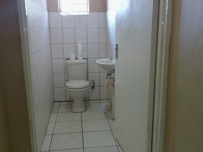 A compact bathroom featuring a standard toilet, pedestal basin, and tiled finishes, requiring minor cosmetic updates to improve its overall presentation.