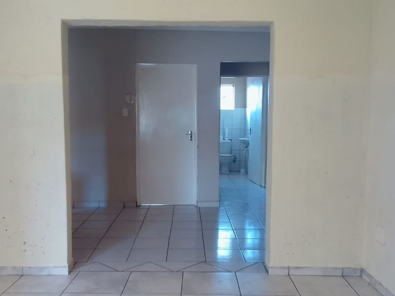 An empty living area featuring tiled flooring and a view through to an internal hallway and bathroom.