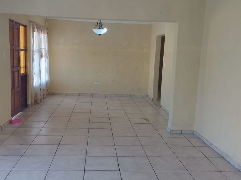 An empty, open-plan living area featuring neutral tiled flooring and a central ceiling light fixture, ready for personalization.