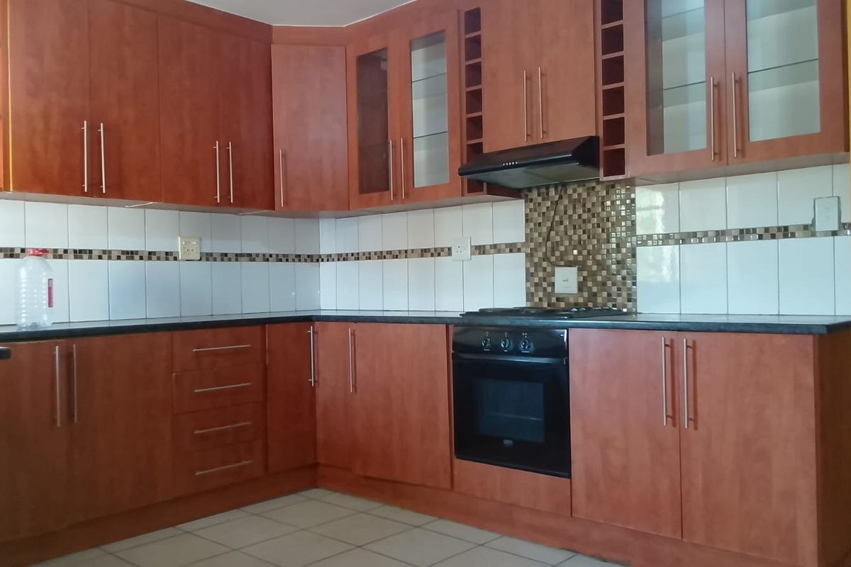 A functional kitchen featuring wood-finish cabinetry, dark countertops, a tiled backsplash, and integrated appliances including an oven and extractor fan.