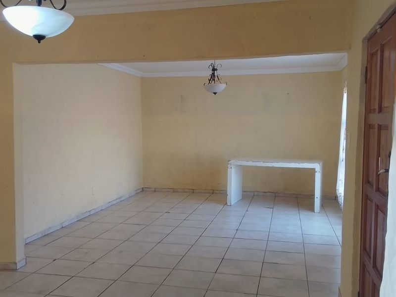 An empty, open-plan living area featuring tiled flooring, cove cornicing, and a built-in concrete console, requiring cosmetic updates to the wall finishes.