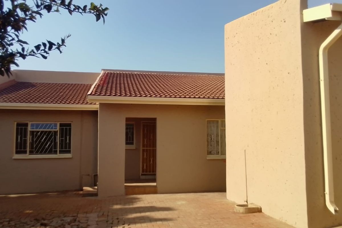 Rear view of the property featuring a paved courtyard, tiled roof, and security bars on the windows.