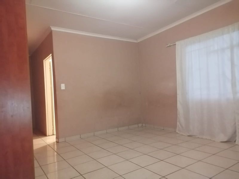 An empty living room featuring tiled flooring, neutral wall paint, and a curtain rail, offering a blank canvas for personalization.
