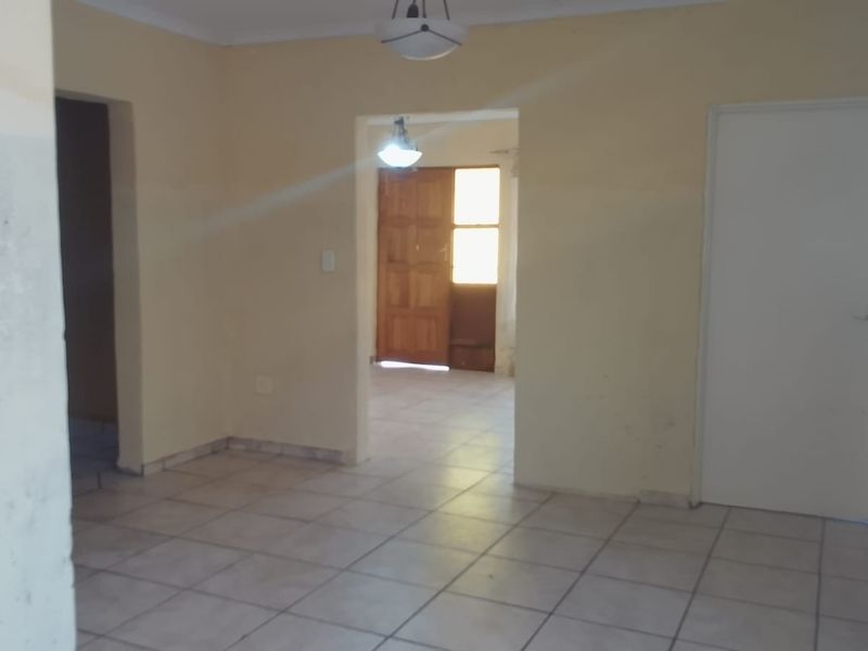 An empty living area featuring tiled flooring, neutral wall paint, and a solid timber door leading to an adjacent space.