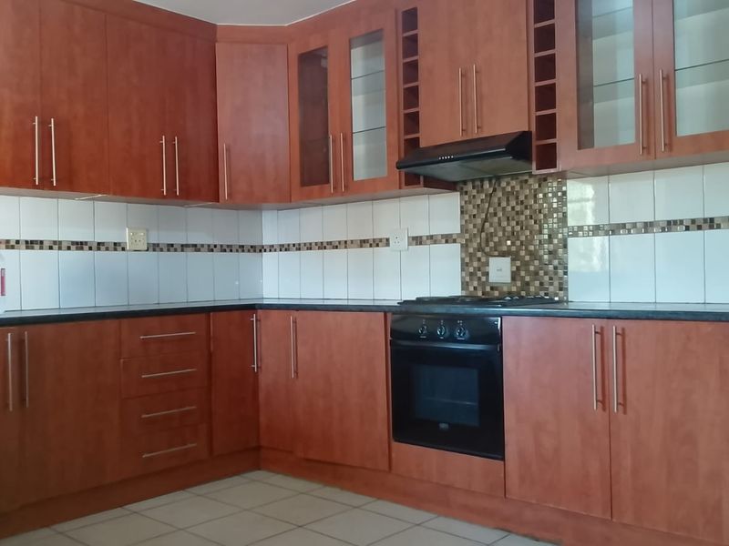 A functional kitchen featuring wood-finish cabinetry, dark countertops, a tiled backsplash, and integrated appliances including an oven and extractor fan.