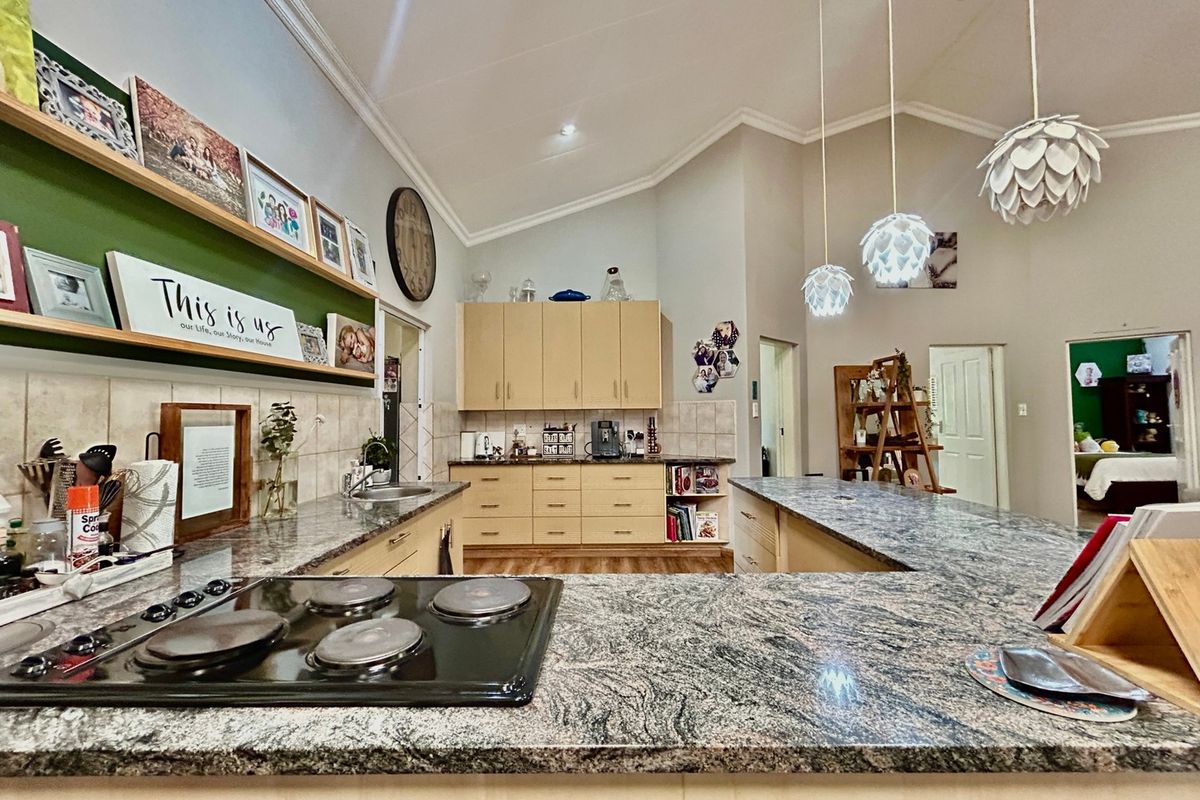 Spacious kitchen featuring granite countertops, ample built-in cabinetry, an electric hob, and a vaulted ceiling with modern pendant lighting.