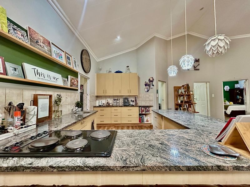 Spacious kitchen featuring granite countertops, ample built-in cabinetry, an electric hob, and a vaulted ceiling with modern pendant lighting.