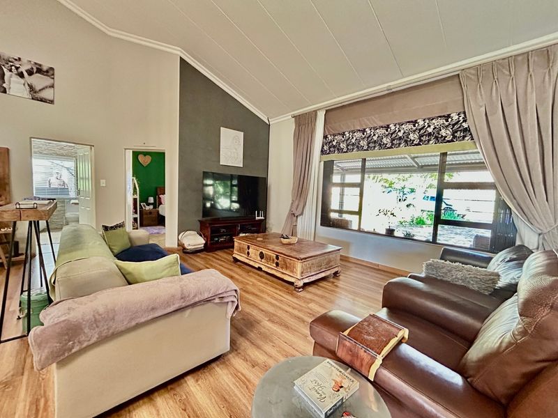 Spacious living room featuring a vaulted ceiling, large picture window providing natural light, and modern laminate flooring with a distinct accent wall.
