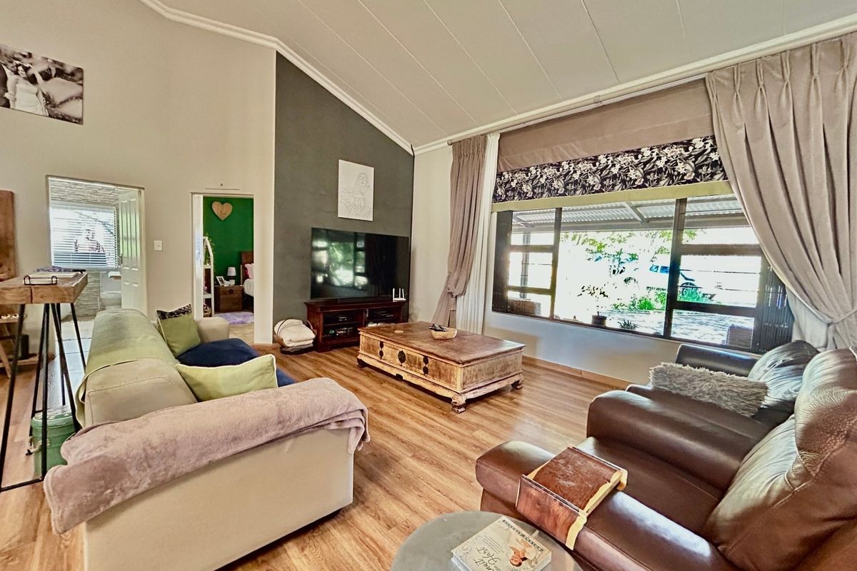 Spacious living room featuring a vaulted ceiling, large picture window providing natural light, and modern laminate flooring with a distinct accent wall.