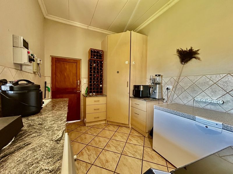 A functional scullery area featuring granite countertops, tiled backsplash, and built-in cabinetry, providing additional workspace and storage adjacent to the main kitchen.