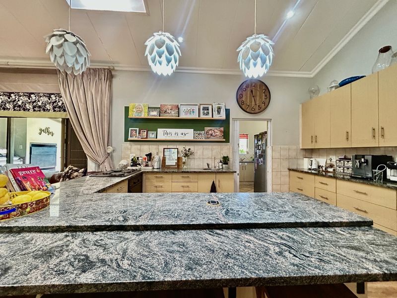 Spacious kitchen featuring extensive granite countertops, ample built-in cabinetry, and a functional layout with a separate scullery area visible in the background.
