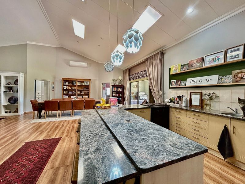 Spacious open-plan living and kitchen area featuring a large granite island, vaulted ceilings with skylights, and modern laminate flooring throughout.