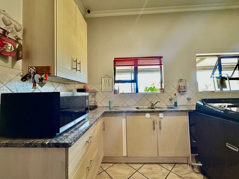A functional kitchen featuring laminate cabinetry, granite-look countertops, a double stainless steel sink, and ceramic tile flooring with a neutral backsplash.