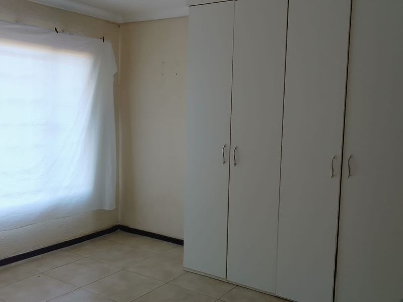 A simple, empty bedroom featuring neutral tiled flooring and white built-in cupboards, offering a clean canvas for personalization.