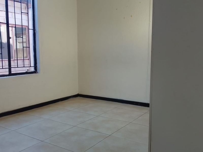 A vacant bedroom featuring neutral tiled flooring and a window fitted with security bars, offering a clean, blank canvas for personalization.