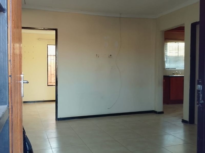 An empty living room featuring tiled flooring and neutral walls, showing signs of wear and exposed wiring, ready for renovation or staging.