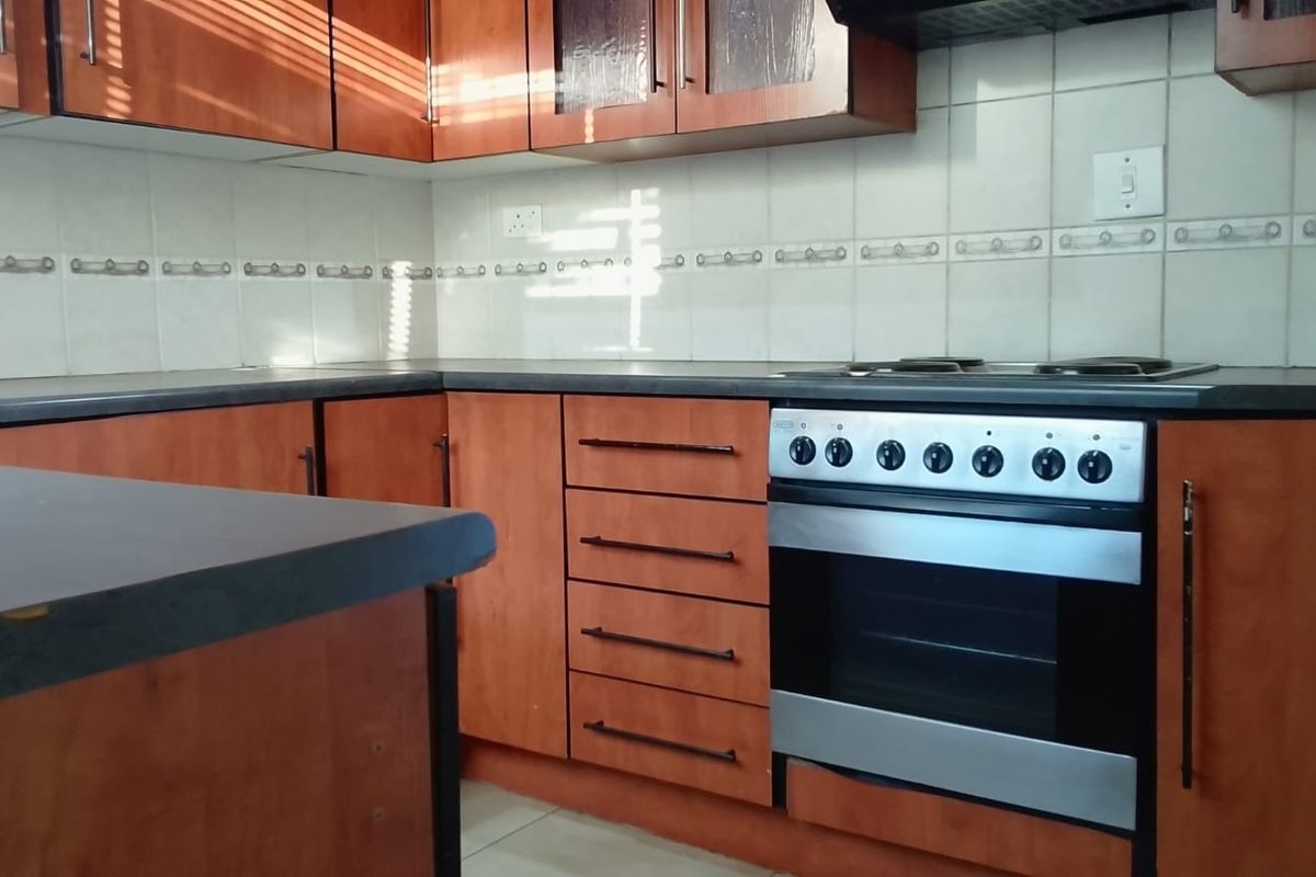 A functional kitchen featuring wood-finish cabinetry, dark laminate countertops, a tiled backsplash, and a built-in oven with a hob.