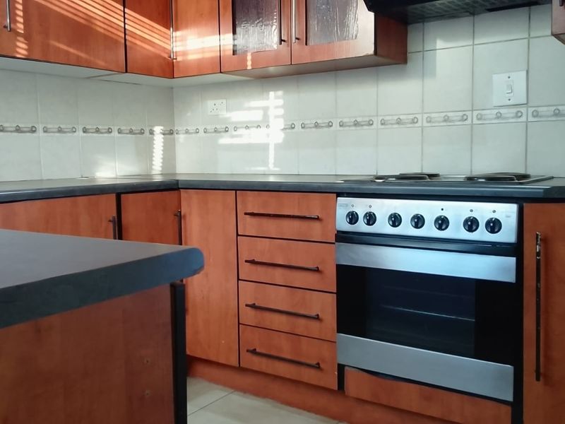 A functional kitchen featuring wood-finish cabinetry, dark laminate countertops, a tiled backsplash, and a built-in oven with a hob.