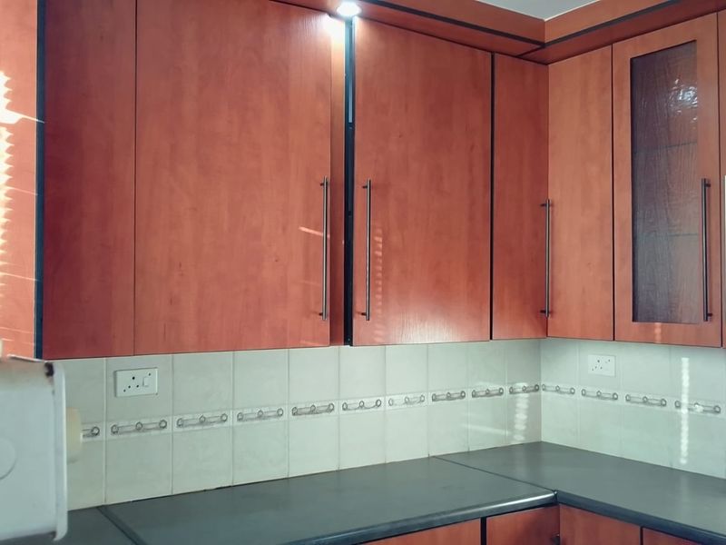 A functional kitchen area featuring wood-look laminate cabinetry, a tiled backsplash, and dark laminate countertops with integrated lighting.
