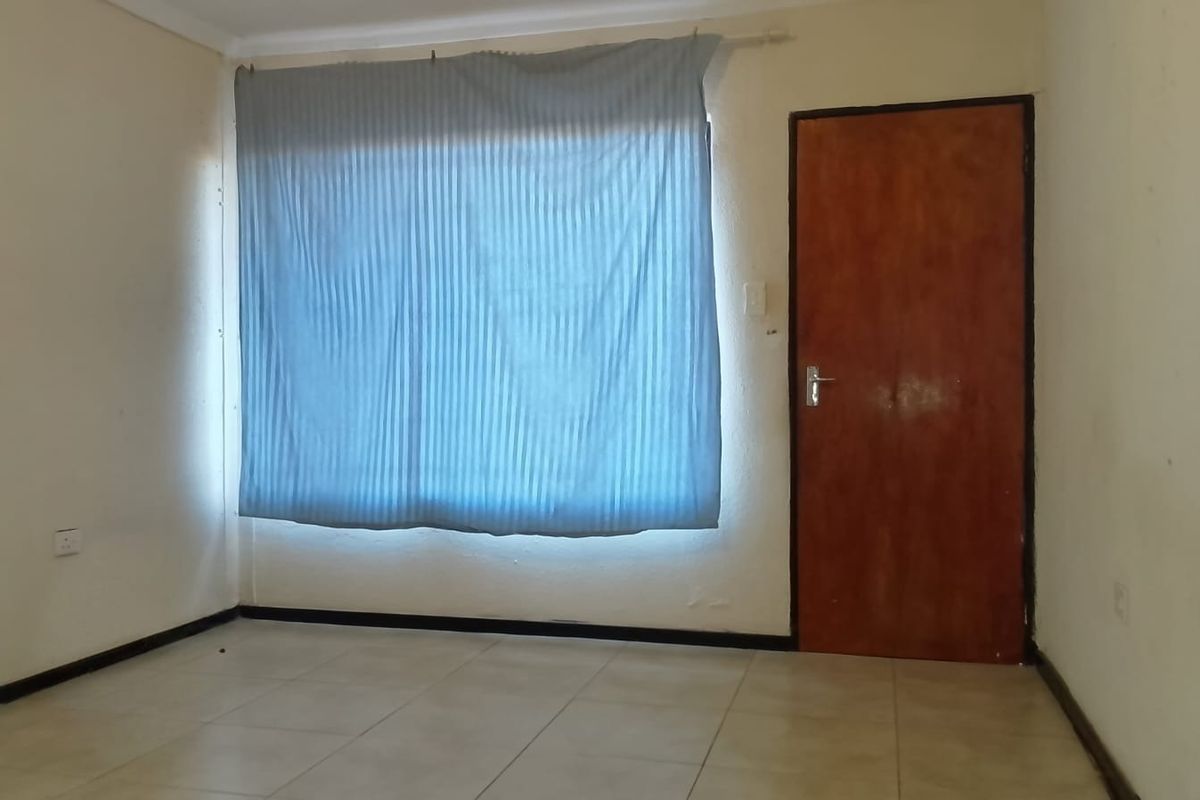 An empty bedroom featuring tiled flooring, coving, and a wooden door, requiring cosmetic updates to improve its overall condition and appeal.