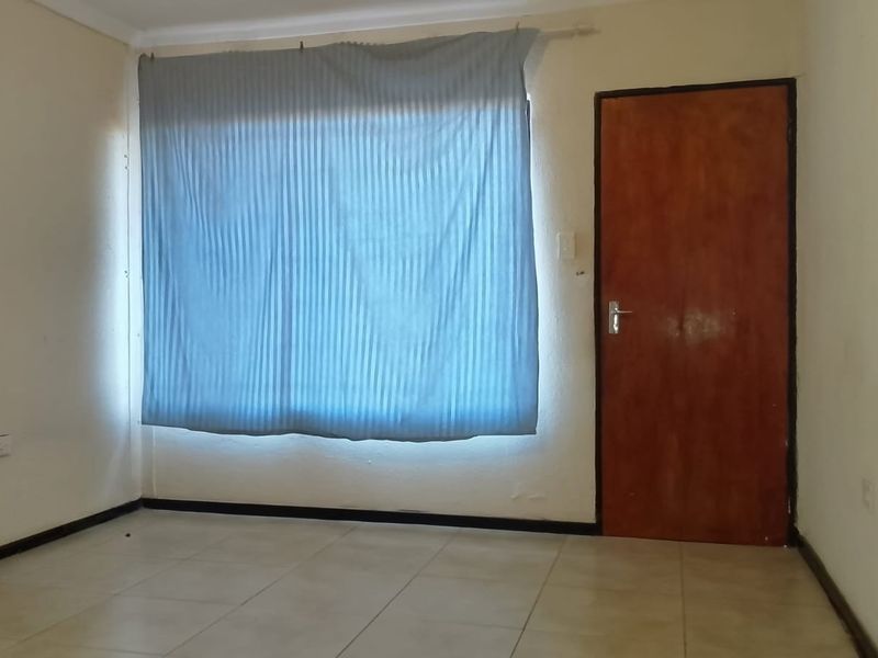 An empty bedroom featuring tiled flooring, coving, and a wooden door, requiring cosmetic updates to improve its overall condition and appeal.