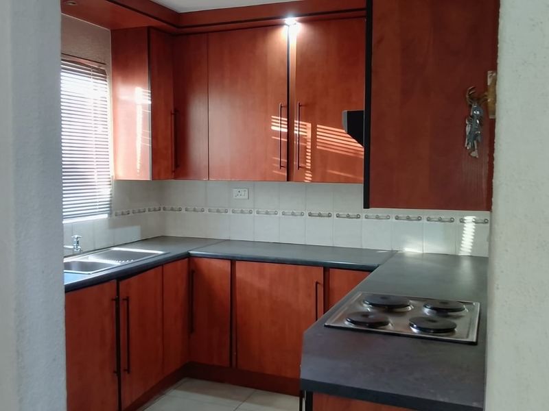A functional kitchen featuring warm-toned laminate cabinetry, dark countertops, a built-in electric hob, and a stainless steel sink with a tiled backsplash.