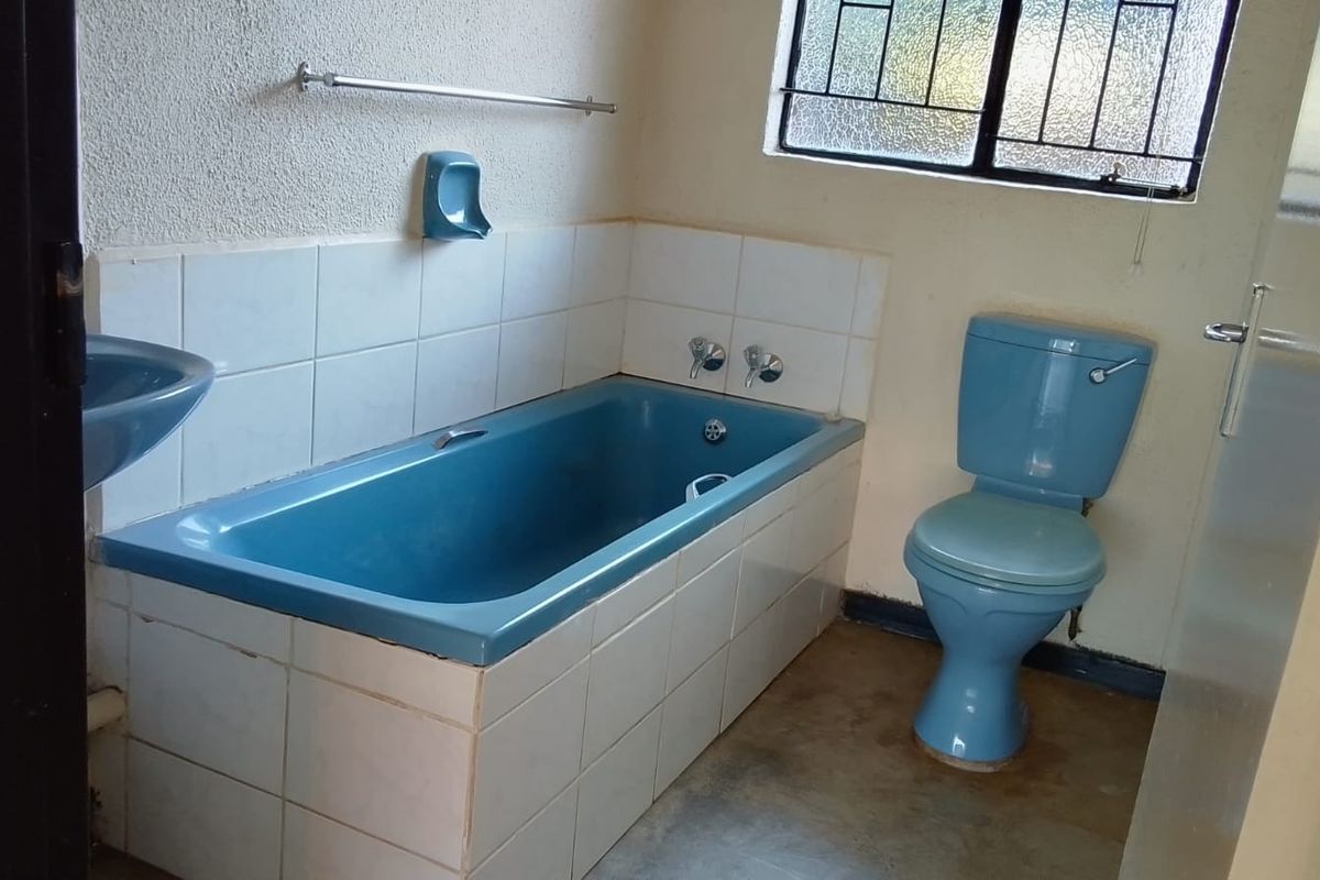 A functional bathroom featuring a built-in bathtub, toilet, and washbasin with dated blue sanitaryware and tiled splashbacks.
