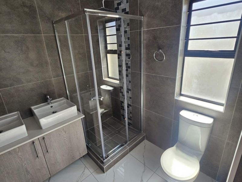 Modern bathroom featuring a double vanity, glass-enclosed shower with rain shower head, and contemporary floor-to-ceiling wall tiling.