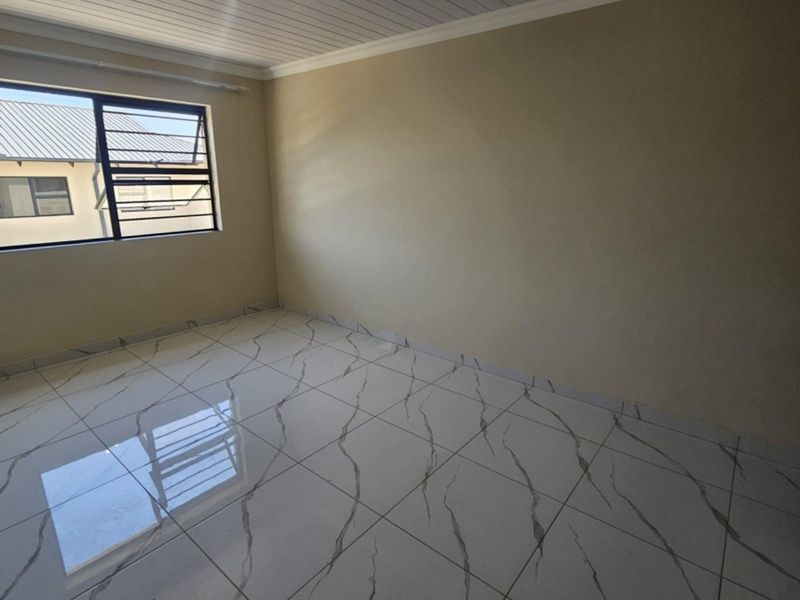 A bright, empty bedroom featuring modern marble-look tiled flooring, a white tongue and groove ceiling, and track lighting.