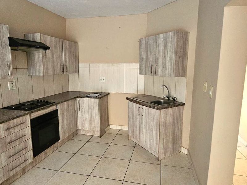 A functional kitchen featuring light wood-grain cabinetry, granite-look countertops, a built-in oven with gas hob, and tiled flooring throughout.