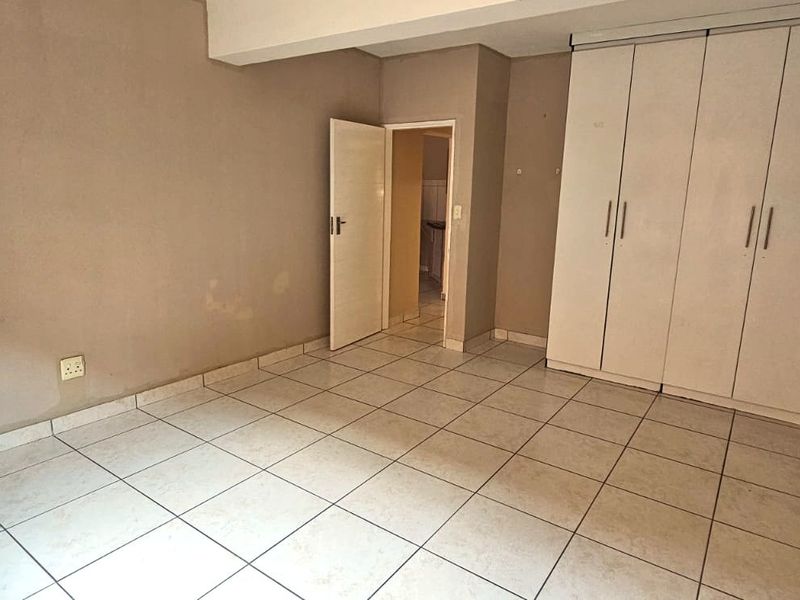 An empty bedroom featuring tiled flooring and a large built-in wardrobe, requiring minor cosmetic updates to the wall finishes.