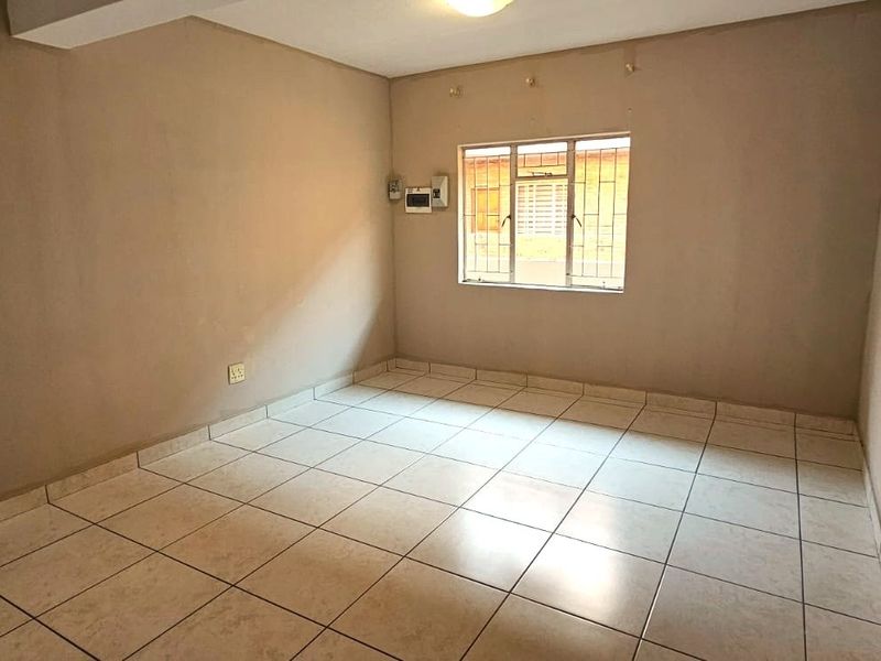 An empty bedroom featuring tiled flooring, a window with security bars, and a wall-mounted electrical distribution board.